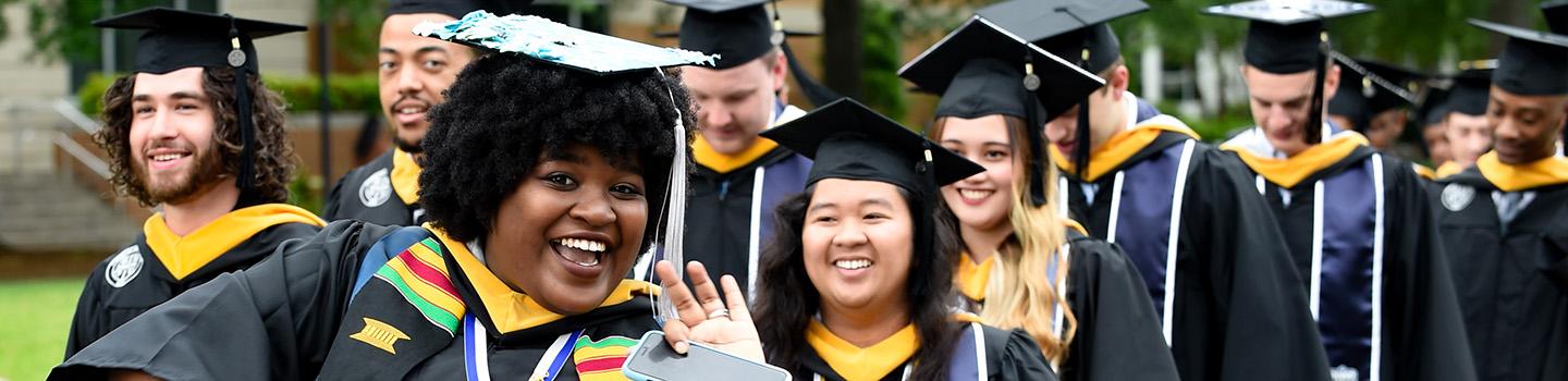 Black female graduate waves at photographer in procession